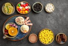 top-view-sweets-table-bowls-berries-chocolate-citrus-fruits-colorful-sweets-plate-cupcakes-cup-herbal-tea-with-cinnamon-sticks-dark-table_140725-111798-3119720