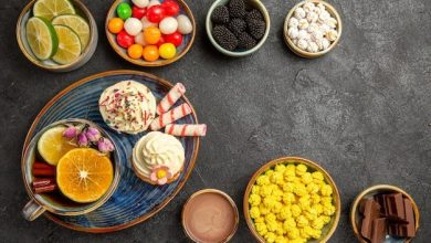 top-view-sweets-table-bowls-berries-chocolate-citrus-fruits-colorful-sweets-plate-cupcakes-cup-herbal-tea-with-cinnamon-sticks-dark-table_140725-111798-3119720